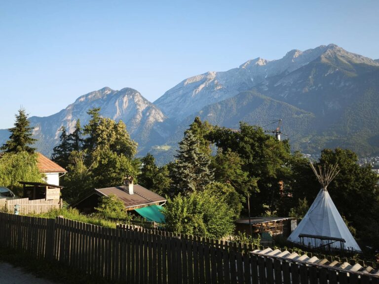A photograph of houses, tents and trees in the foreground, and moutains in the background